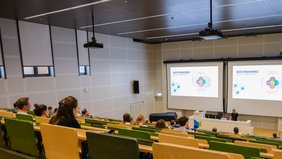 Eine Person, in Totale, referiert in einem Hörsaal. 