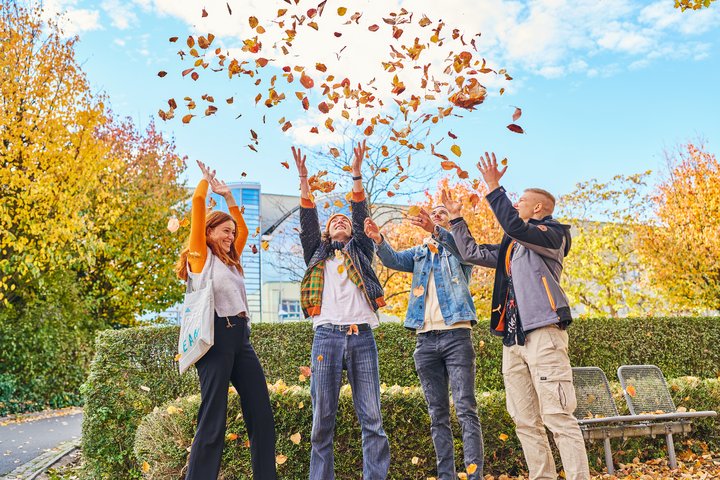 Junge Menschen auf einem herbstlichem Campus, die werfen Herbstlaub in die Luft