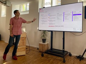 Ein Referent steht links neben einem Smartboard und zeigt.