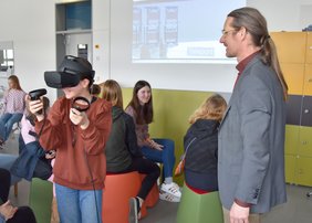 Prof. Christian Erfurth aus dem Fachbereich Wirtschaftsingenieurwesen testet mit Schülerinnen die Darstellung einer virtuellen Umgebung mit einer VR-Brille