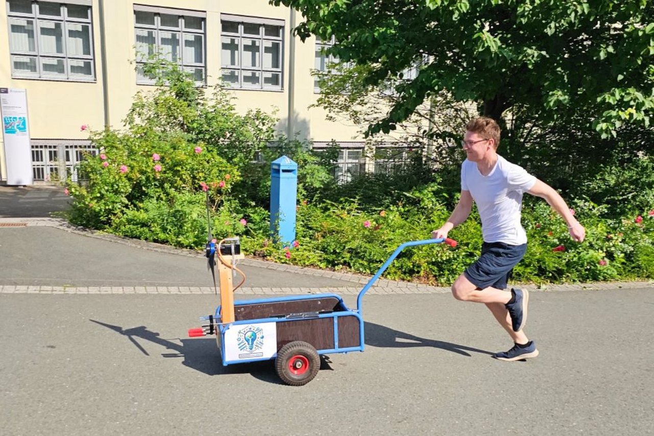 Studierender der einen Wagen mit einem Windrad anschiebt.