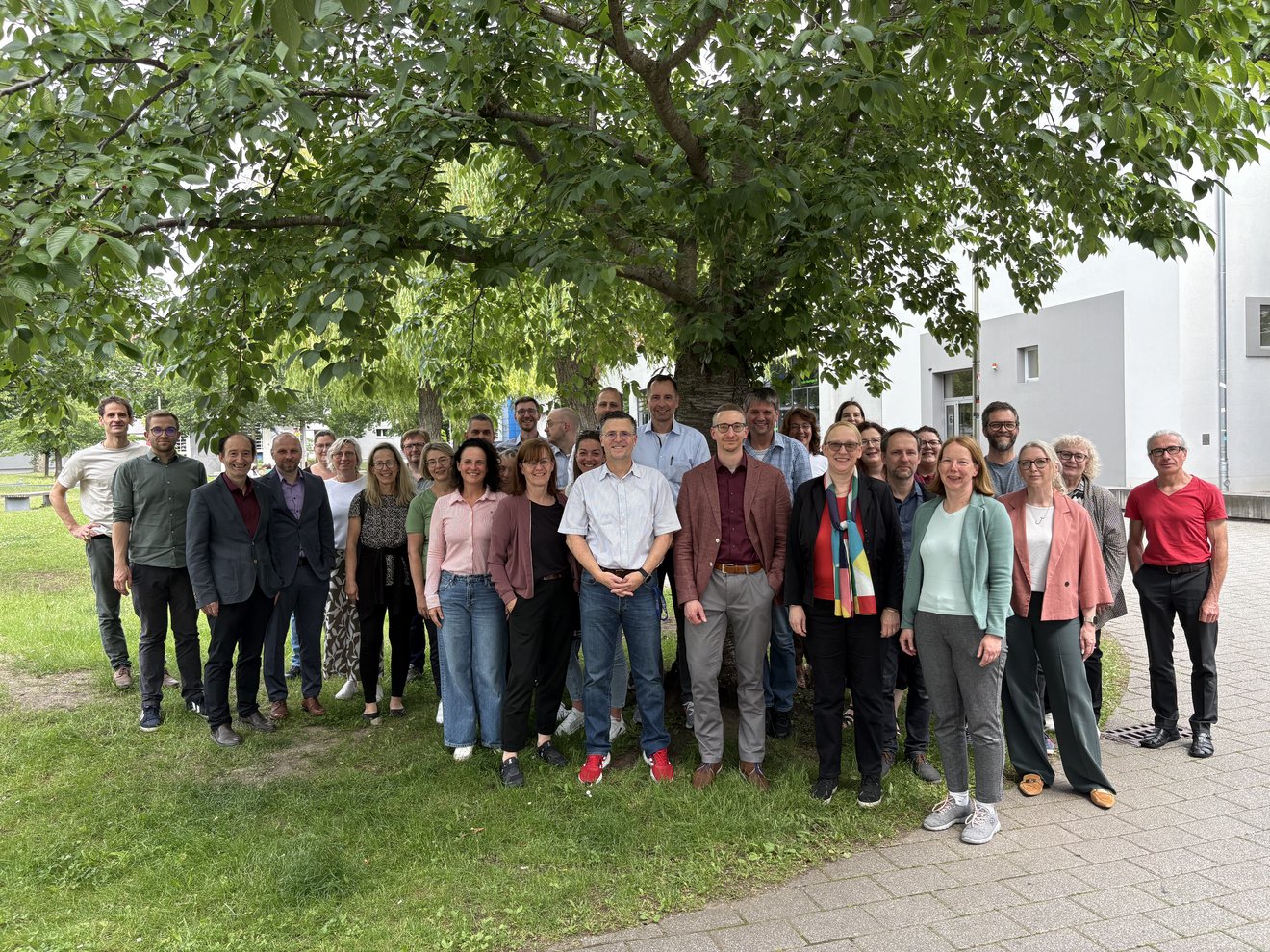 Etwa 40 Personen stehen unter einem Baum und schauen in die Kamera