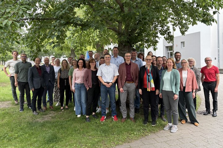 Etwa 40 Personen stehen unter einem Baum und schauen in die Kamera