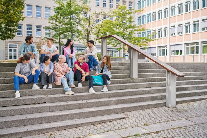 Gruppe von jungen Menschen sitzt auf den Treppenstufen vor einem größeren Gebäude