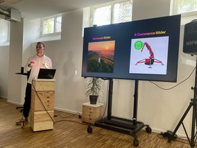 Ein Referent steht hinter einem Pult links neben einem Smartboard und spricht.