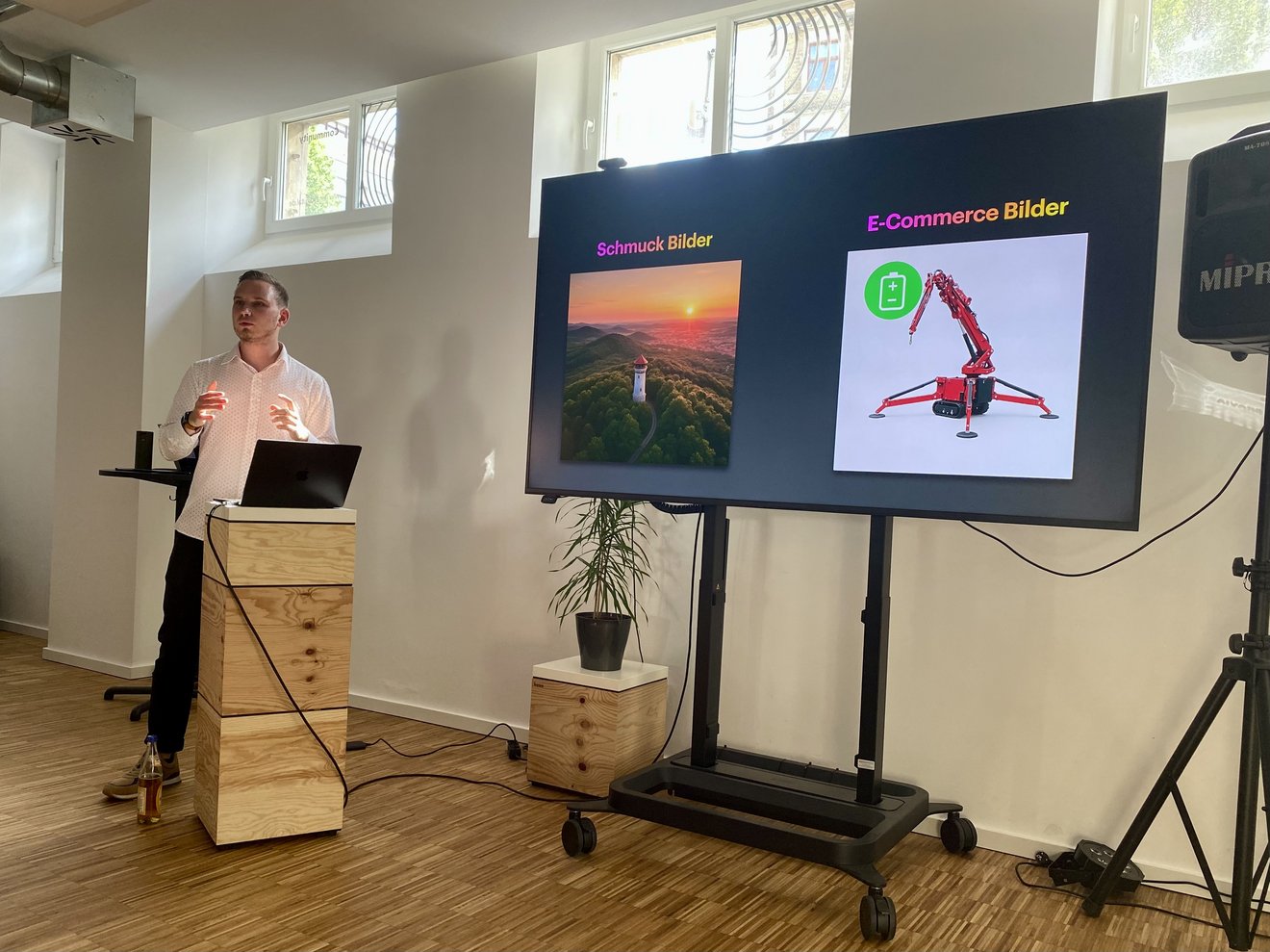 Ein Referent steht hinter einem Pult links neben einem Smartboard und spricht.