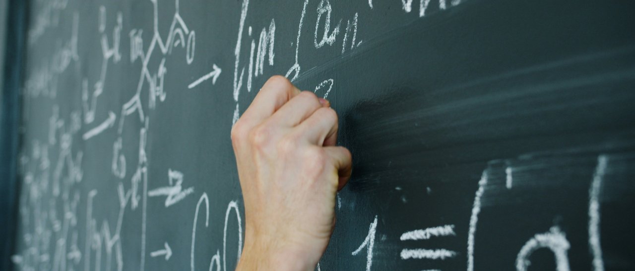 Eine Person schreibt mathematische Formeln auf eine Tafel