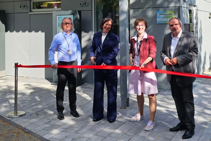 4 Personen stehen vor einem Gebäude und sind bereit, ein rotes Band zu durchschneiden.