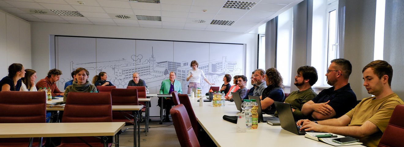 Menschen sitzen an Tischen in einem Seminarraum und warten auf den Beginn der Veranstaltung.