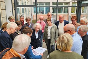 Gruppe von Menschen um eine Mappe mt historischen Aufnahmen vom Campus gebeugt
