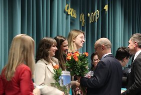 Absolventinnen erhalten eine Zeugnismappe und Blumen.