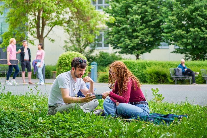 Eine junge Frau und ein junger Mann sitzen im Grünen und scheuen gemeinsam auf ein Handy.