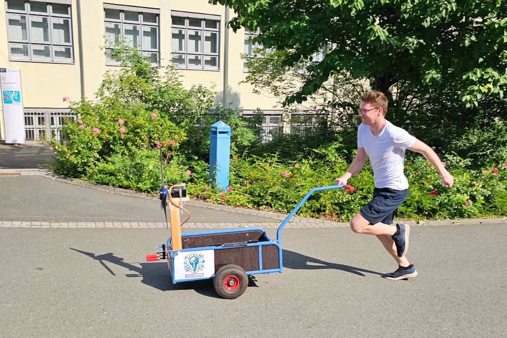 Studierender der einen Wagen mit einem Windrad anschiebt.
